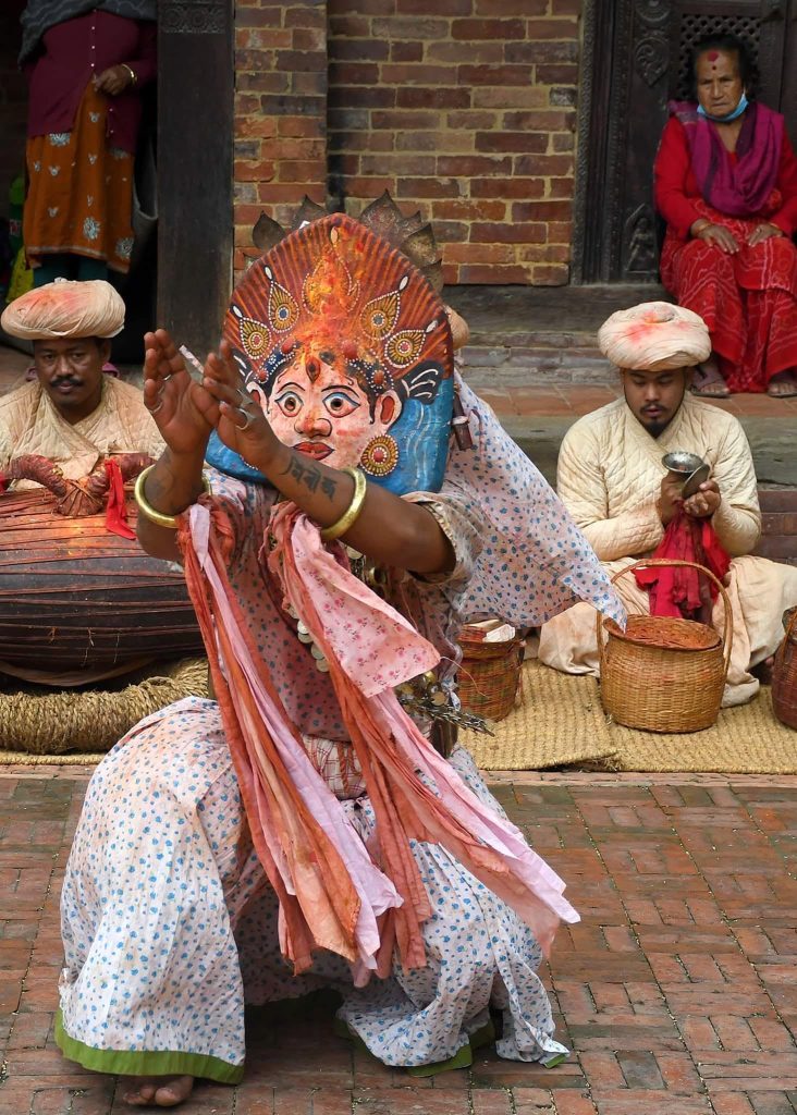 Masked dancer in a courtyard in Patan during the Mohani period, crowd pressed against the temple plinth