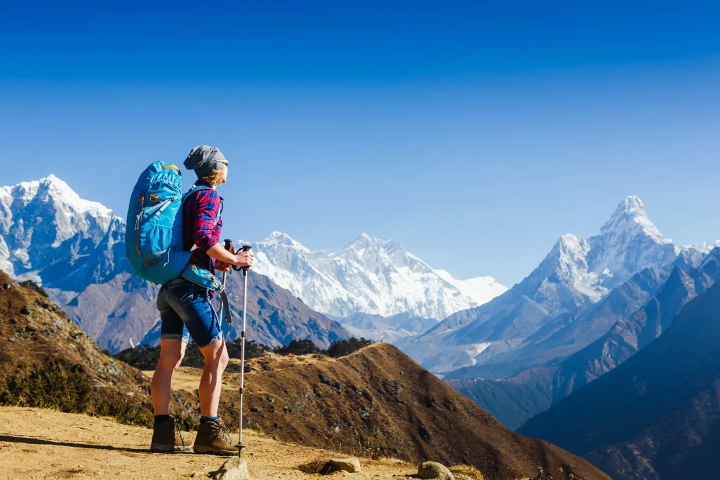 Trekking poles leaning against a teahouse wall with worn boots and a daypack beside them