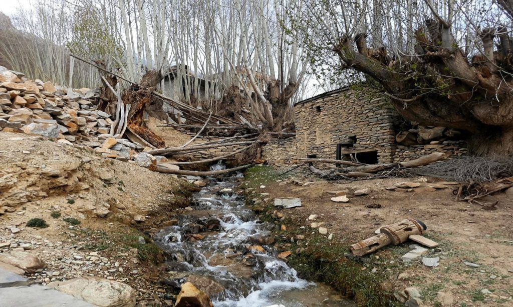 Stone-lined irrigation channel carrying meltwater along a dry hillside above terraced fields