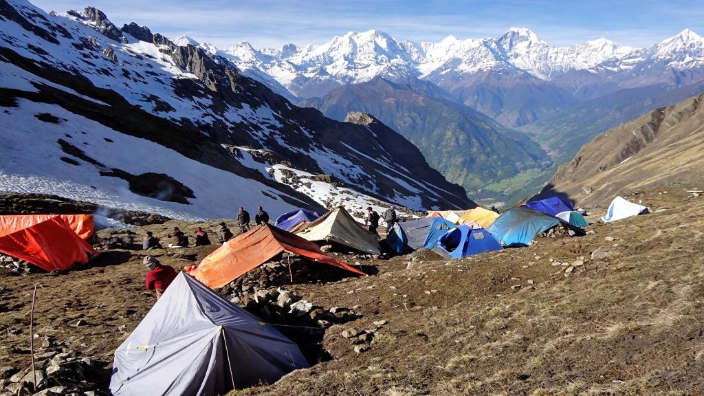 Temporary tents clustered on a high pasture during the collection season with snow on nearby slopes