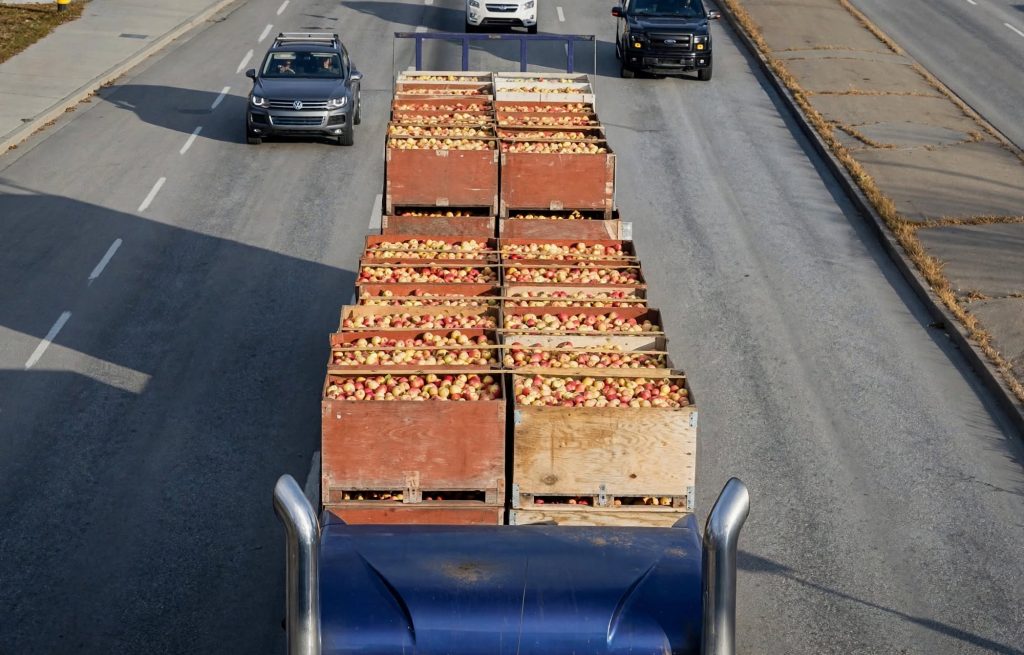 Crates of freshly picked apples loaded for transport beside a dusty mountain road