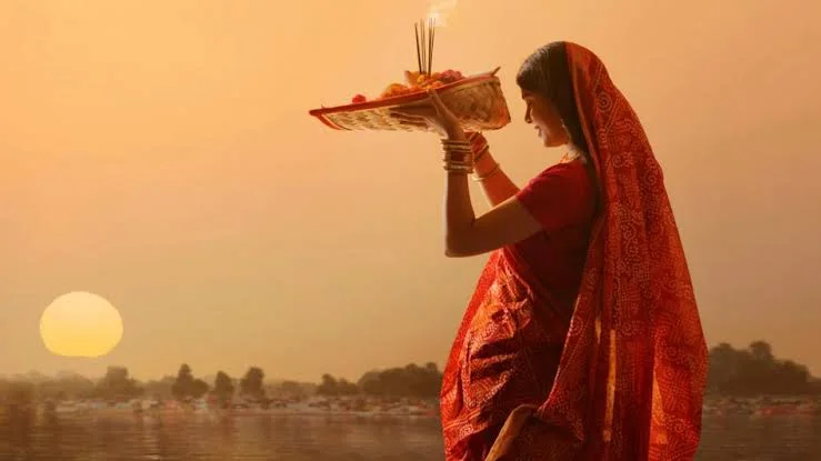 Woman performing Chhath Puja arghya offering to the rising sun near a riverbank.