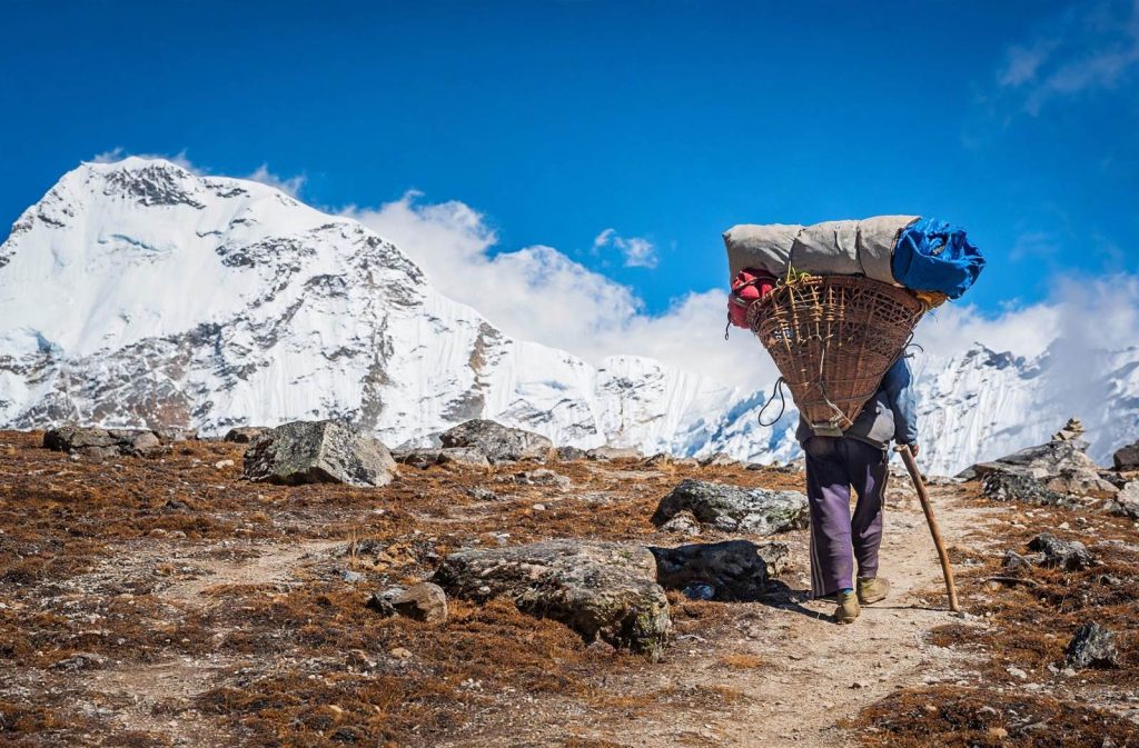 Porter carrying sorted recyclables down a stone trail toward Lukla